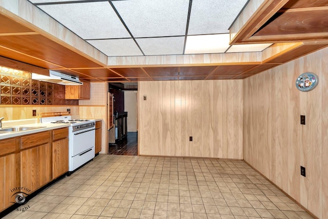 kitchen with light countertops, gas range gas stove, range hood, a sink, and wooden walls