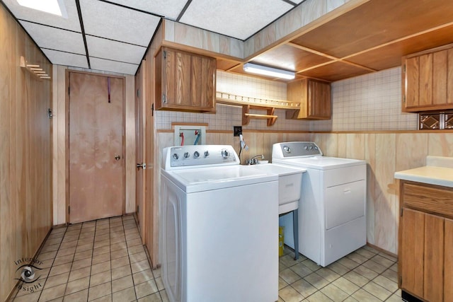 laundry room featuring washing machine and clothes dryer, wood walls, a sink, cabinet space, and light tile patterned floors