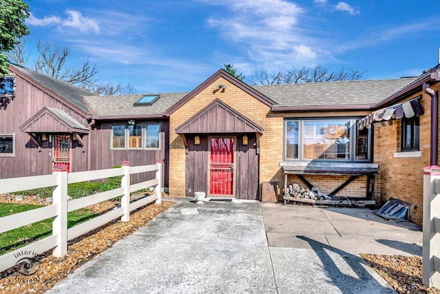 view of front facade featuring board and batten siding, brick siding, a fenced front yard, and roof with shingles