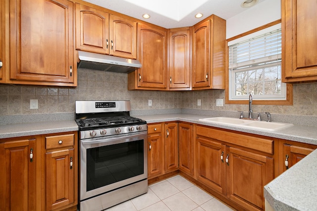 kitchen featuring a sink, brown cabinetry, under cabinet range hood, and gas stove