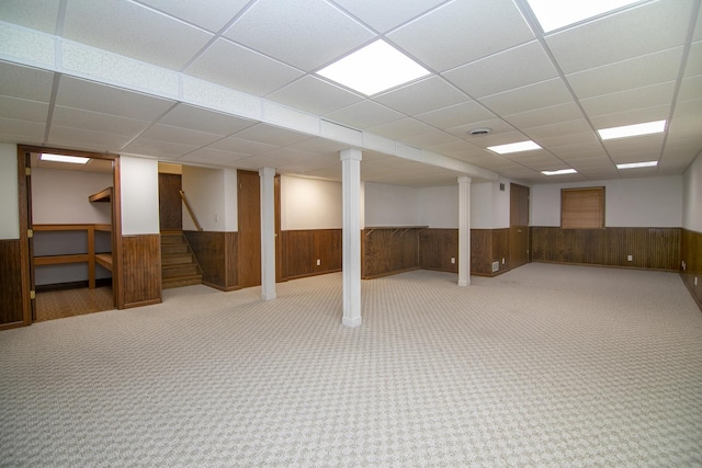 finished basement featuring carpet flooring, wooden walls, a drop ceiling, and wainscoting