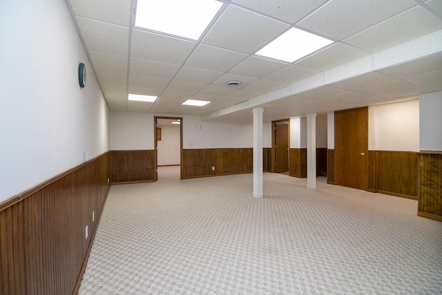 finished basement featuring visible vents, wood walls, a drop ceiling, and wainscoting
