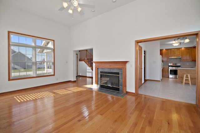 unfurnished living room featuring light wood-style flooring, baseboards, a fireplace, a ceiling fan, and a high ceiling