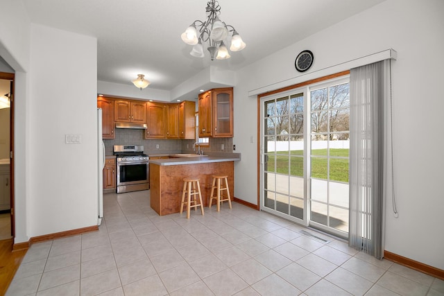 kitchen featuring decorative backsplash, stainless steel range with gas stovetop, brown cabinets, under cabinet range hood, and a sink