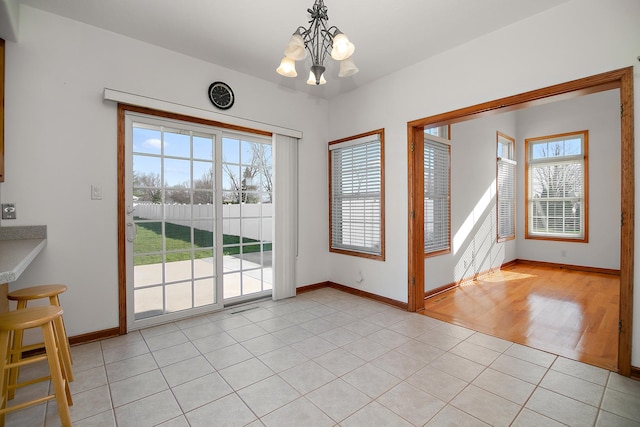 doorway with baseboards, a chandelier, and light tile patterned floors