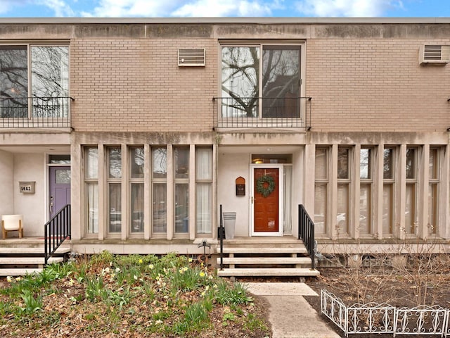 view of exterior entry featuring a balcony, brick siding, and a wall mounted air conditioner