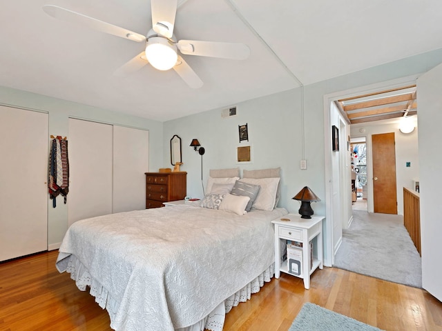 bedroom featuring two closets, wood finished floors, ceiling fan, and visible vents