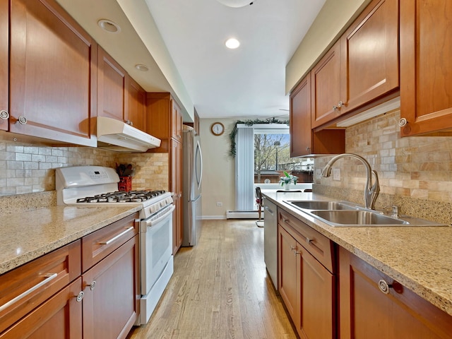 kitchen featuring a sink, appliances with stainless steel finishes, brown cabinets, light wood-type flooring, and under cabinet range hood
