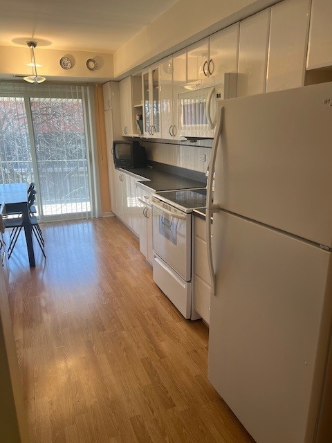 4901 Golf Rd Unit 405, Skokie, IL 60077 - kitchen with white appliances, glass insert cabinets, dark countertops, white cabinets, and light wood finished floors