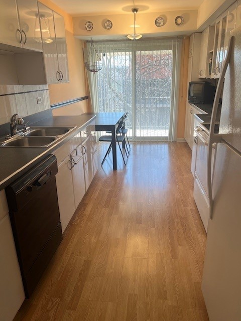 4901 Golf Rd Unit 405, Skokie, IL 60077 - kitchen featuring light wood-style floors, freestanding refrigerator, white cabinetry, black dishwasher, and a sink