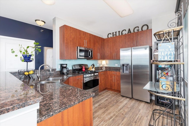 kitchen with brown cabinets, a sink, a peninsula, stainless steel appliances, and light wood-style flooring