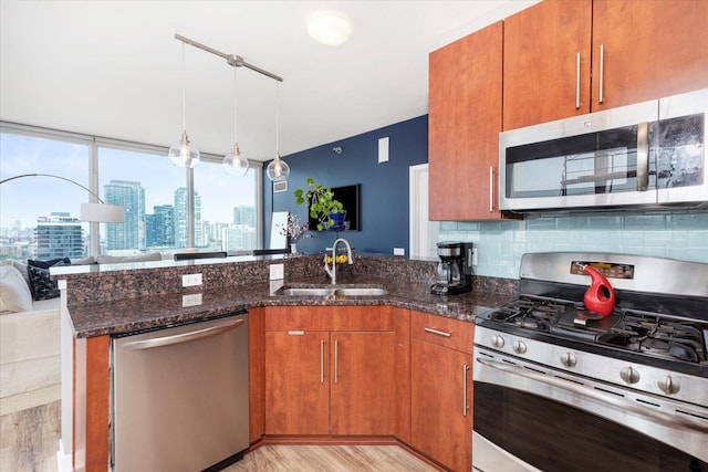 kitchen with brown cabinets, a sink, open floor plan, dark stone counters, and stainless steel appliances