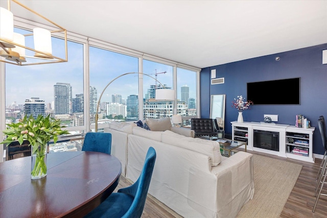 living area with a glass covered fireplace, floor to ceiling windows, wood finished floors, and visible vents