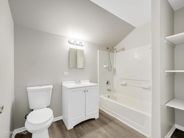 bathroom with toilet, vaulted ceiling, wood finished floors, washtub / shower combination, and vanity