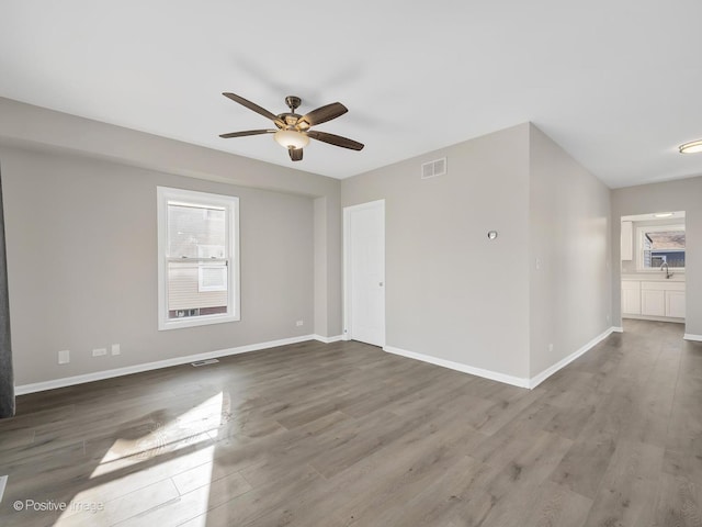 spare room with wood finished floors, visible vents, a ceiling fan, and baseboards