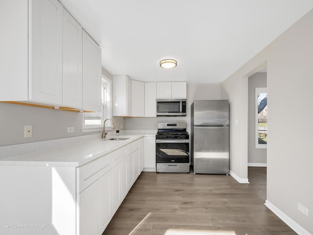 kitchen featuring a sink, light countertops, white cabinets, baseboards, and appliances with stainless steel finishes