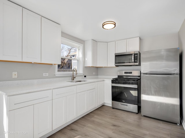 kitchen featuring light wood finished floors, stainless steel appliances, light countertops, a sink, and white cabinetry