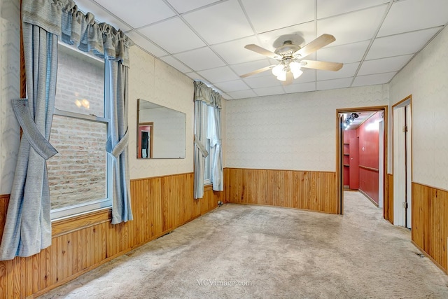 unfurnished room with a drop ceiling, carpet floors, wood walls, and wainscoting