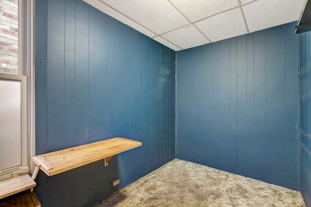 carpeted spare room with wooden walls and a paneled ceiling
