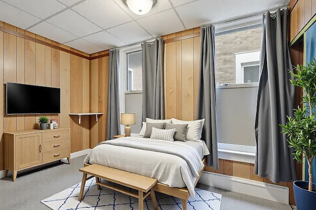 bedroom with light carpet, wood walls, and a paneled ceiling