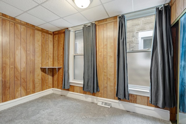 unfurnished room with visible vents, wood walls, carpet, and a paneled ceiling
