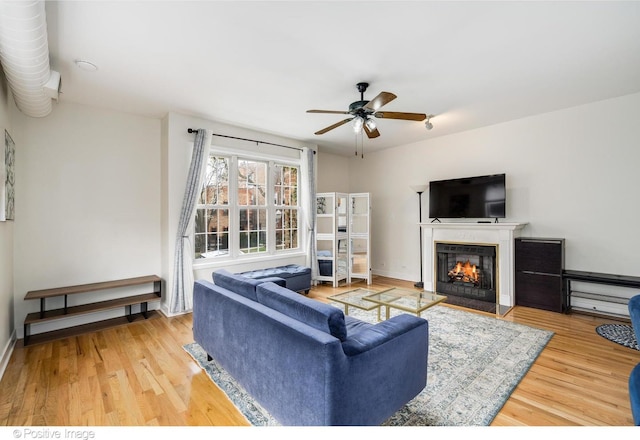 living room featuring baseboards, wood finished floors, a ceiling fan, and a glass covered fireplace