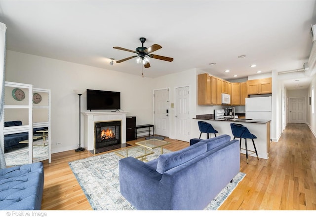 living area with a ceiling fan, a fireplace with flush hearth, light wood-type flooring, baseboards, and recessed lighting