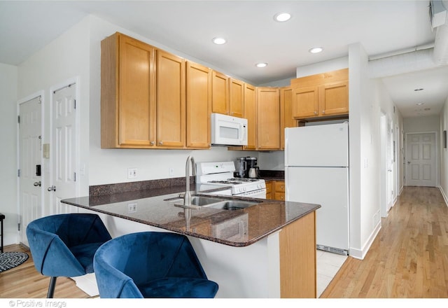 kitchen with a peninsula, dark stone countertops, a kitchen breakfast bar, white appliances, and recessed lighting