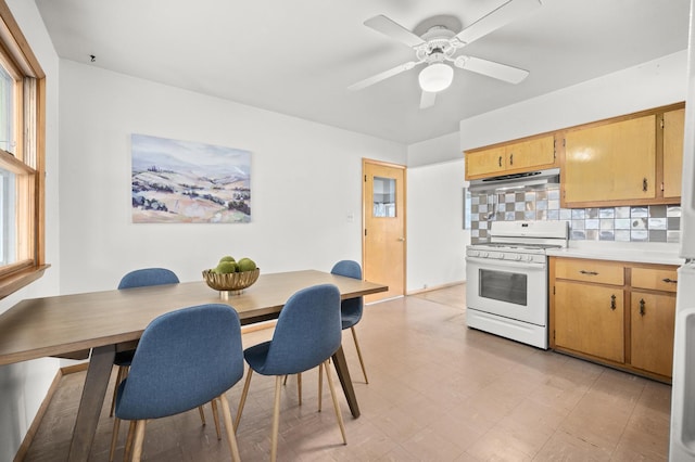 kitchen featuring light countertops, a ceiling fan, under cabinet range hood, white range with gas stovetop, and decorative backsplash