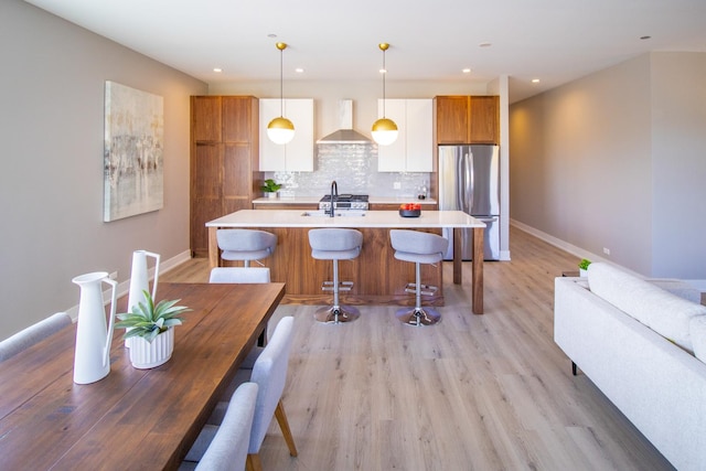 kitchen featuring light countertops, freestanding refrigerator, wall chimney range hood, and baseboards