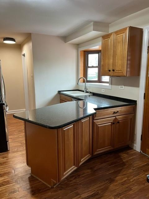 1911 N 73rd Ave N, Elmwood Park, IL 60707 - kitchen featuring dark wood-style flooring, a peninsula, brown cabinets, and dark stone counters