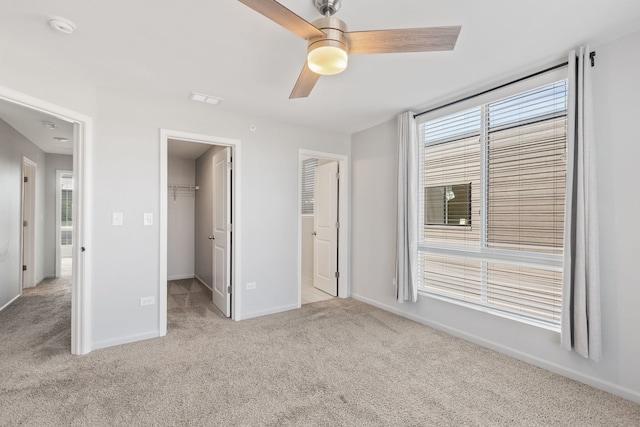 unfurnished bedroom with a closet, baseboards, a ceiling fan, a walk in closet, and light carpet