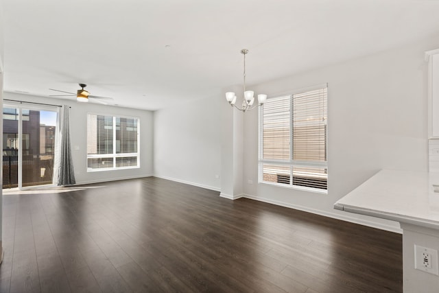 unfurnished dining area featuring dark wood-type flooring, ceiling fan with notable chandelier, and baseboards