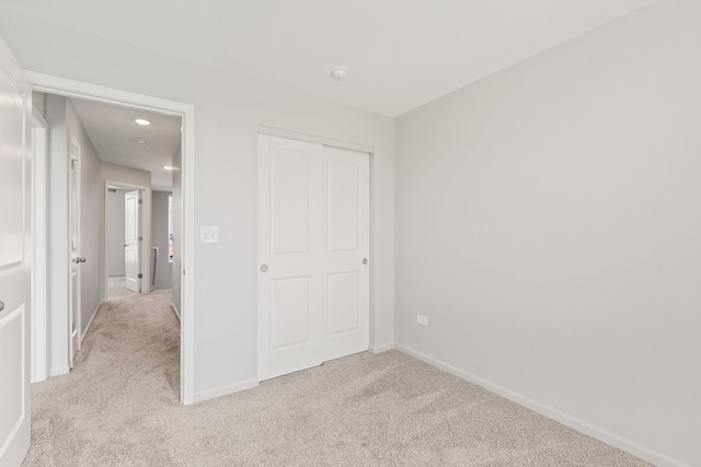 unfurnished bedroom with a closet, baseboards, and light colored carpet
