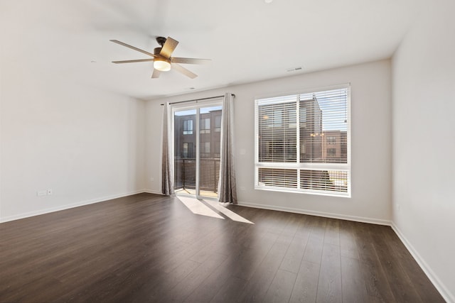 unfurnished room featuring baseboards, dark wood-style flooring, visible vents, and a ceiling fan