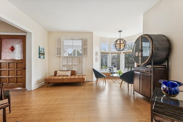 living area with baseboards, an inviting chandelier, and light wood-type flooring