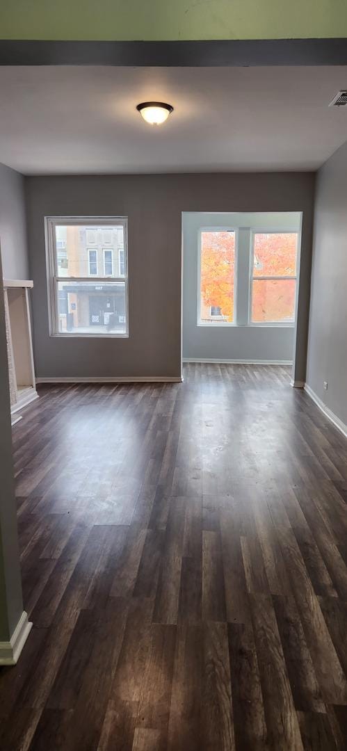 unfurnished living room featuring dark wood-style flooring, baseboards, and visible vents