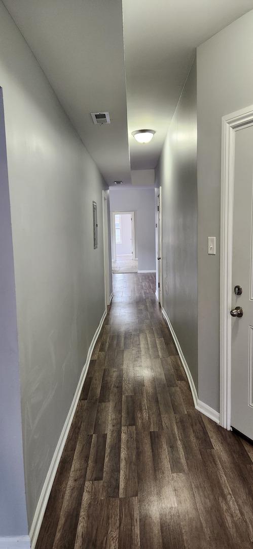 hall featuring visible vents, baseboards, and dark wood finished floors