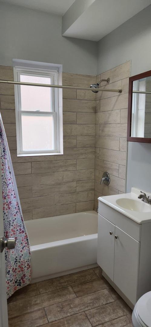 bathroom with wood tiled floor, toilet, vanity, and shower / bath combination with curtain