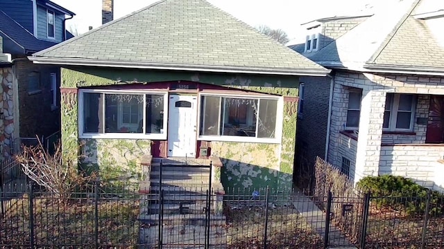 bungalow featuring a fenced front yard, roof with shingles, and a chimney