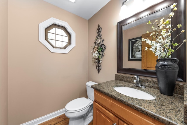 bathroom featuring vanity, baseboards, wood finished floors, and toilet