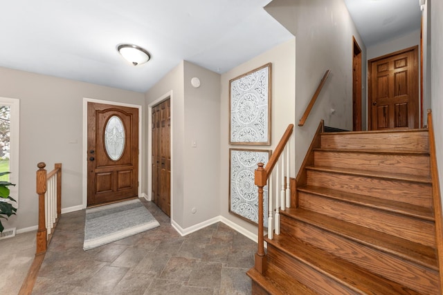 foyer with stairway, baseboards, stone finish floor, and visible vents