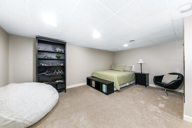 bedroom with baseboards, a drop ceiling, and light carpet