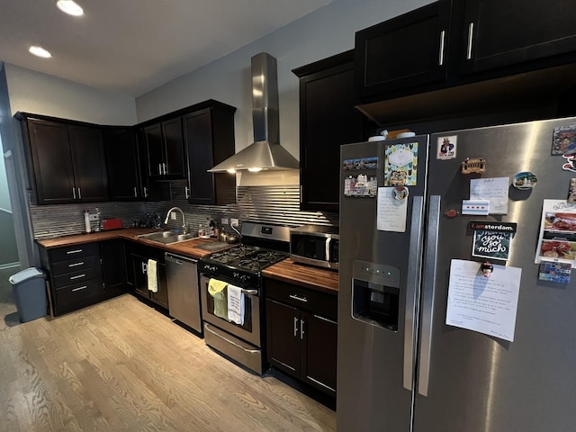 kitchen featuring a sink, wall chimney exhaust hood, dark cabinetry, and appliances with stainless steel finishes