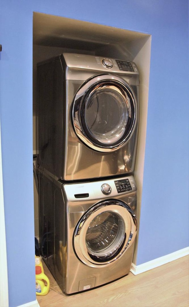 laundry area featuring baseboards, stacked washer / dryer, laundry area, and wood finished floors