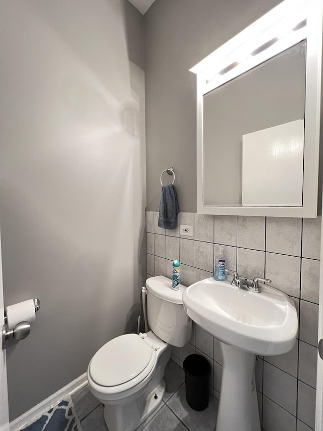 bathroom with baseboards, toilet, tile patterned flooring, and tile walls