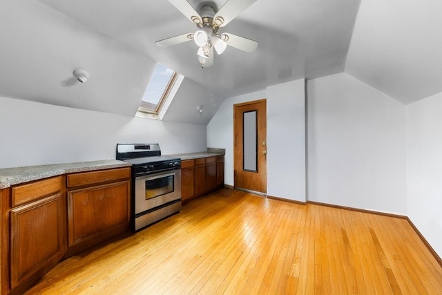 kitchen featuring lofted ceiling with skylight, brown cabinets, light wood-type flooring, and stainless steel gas stove
