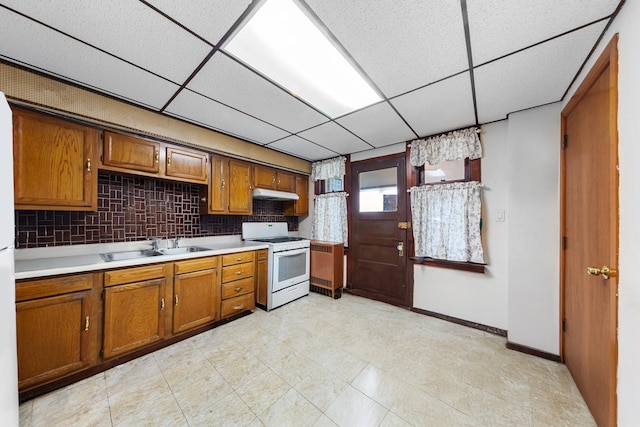 kitchen featuring under cabinet range hood, light countertops, brown cabinets, white gas stove, and a paneled ceiling