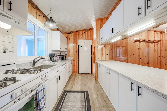 kitchen with light countertops, wooden walls, under cabinet range hood, white appliances, and light wood-style floors