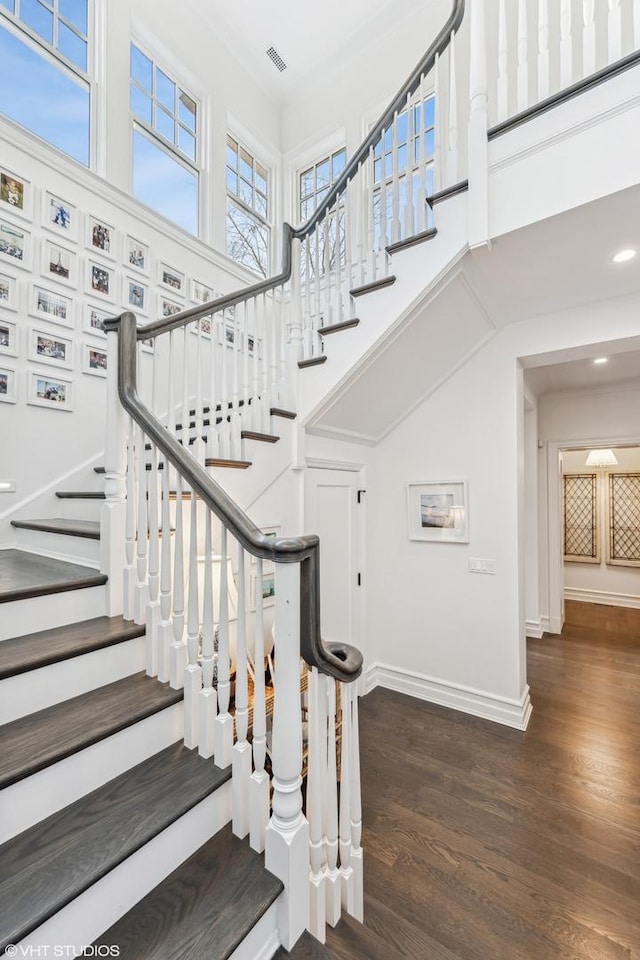 stairs featuring a towering ceiling, wood finished floors, and baseboards